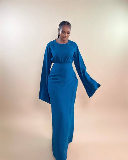 A woman modeling a blue maxi dress with a faux wrap design and bell sleeves.