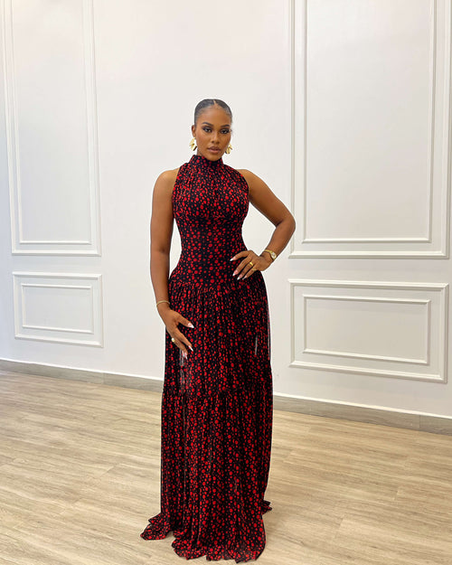 Woman in a red and black patterned dress standing against a white paneled wall.