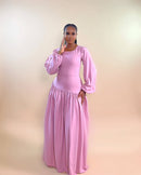 A model wearing a pink maxi dress with a fitted bodice, long puffed sleeves, and a gathered skirt.