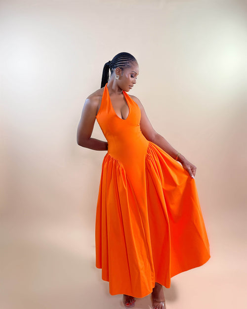 A model wearing an orange sleeveless halter neckline dress with a plunging V-cut and a pleated skirt.