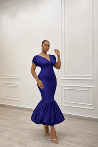 Woman wearing a blue dress standing against a white paneled wall.