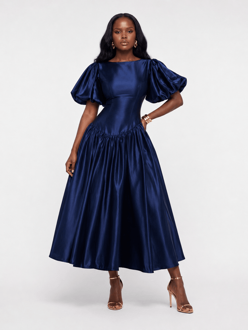 Woman wearing a navy blue satin dress with puff sleeves on a white background
